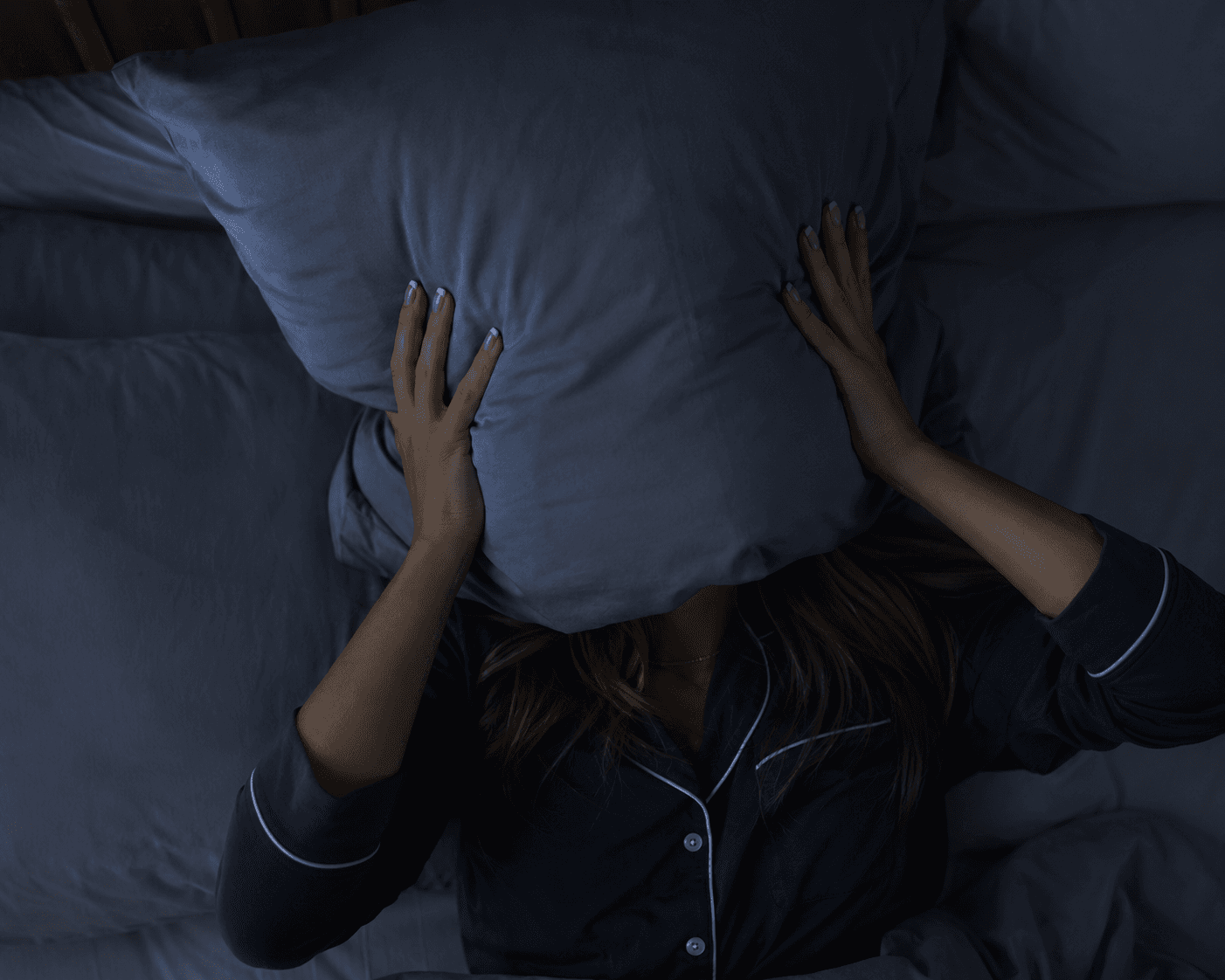 A restless person covering their face with a pillow in bed.